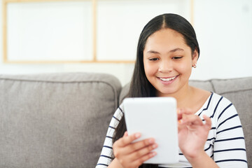 Obraz premium Dipping into the digital world. Shot of a happy young girl relaxing on the sofa and using a digital tablet.