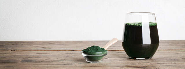 fresh green drink with spirulina in glass, spirulina powder with spoon on wooden background. self...