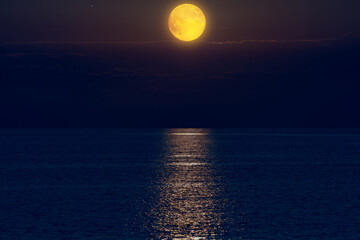 Moon with starry skies above ocean horizon.