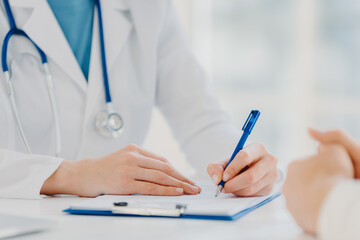 Woman doctor writes down in clipboard, makes prescription for patient, records data for analysis
