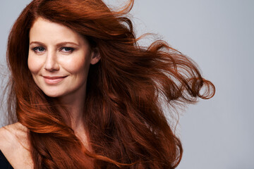Showing off her crowning glory. Studio shot of a young woman with beautiful red hair posing against a gray background.