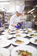 Capable hands in the kitchen. Shot of a chef plating food for a meal service in a professional...