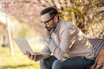 A thoughtful man sits in the park and using laptop.