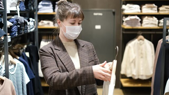 Woman in a medical mask trying on sweater in clothing store.