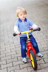 Active blond kid boy in colorful clothes driving balance and learner's bike or bicycle in domestic...
