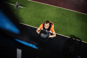 Man in a squatting position holds a medicine ball in the gym. 