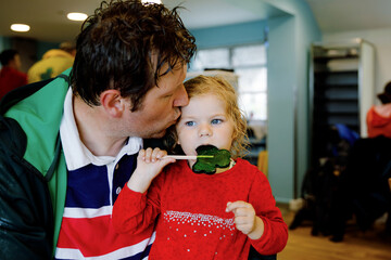 Cute toddler girl and father with cloverleaf lollipop in Irish pub or cafe. Child and dad, young...