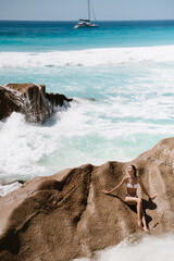 Beautiful young woman in white one-piece swimsuit and sunglasses on Seychelles beach on Mahe or La Digue island