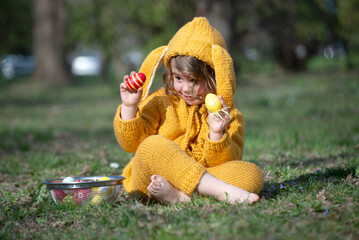Little girl in a rabbit costume is sitting in the park with colorful eggs on Easter day
