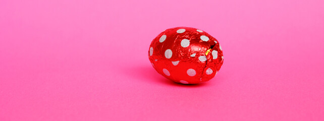 Chocolate egg in colorful foil for Easter on a pink background. The egg is wrapped in red foil. Happy Easter. Chocolate. Sweets for children and adults. Candy. Dessert. Copy space. Top view. Flat lay