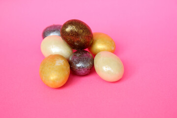 Chocolate eggs on a pink background at Easter. The eggs are multicolored. Happy Easter. Chocolate. Sweets for children and adults. Candy. Dessert. Copy space. View from above. Flat lying down