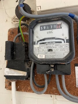 Close-up of a traditional electric meter displaying household electricity usage, with connected electrical cables and wiring mounted on an exterior wall. Useful for energy consumption, electricity sup