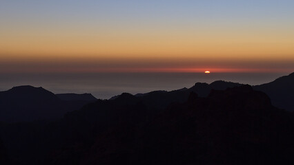 Panoramic view over the rugged mountains of island Gran Canaria, Canary Islands, Spain at sunset with colorful sky and sun going down on the horizon.