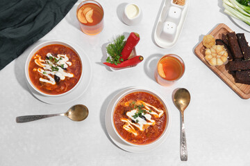 View from above. Laid table for two. Ukrainian red borscht with sour cream in white plates. Nearby fresh herbs, croutons with garlic and compote in glasses