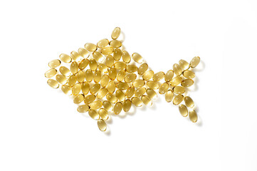 On a white clean background, a fish is laid out from transparent golden omega 3 capsules