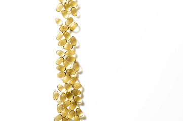 A path of transparent golden omega 3 capsules is laid out on a white clean background.
