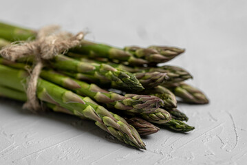 Close-up, horizontal frame. On a gray beautiful background lies a bunch tied with twine, fresh green asparagus