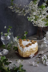 Beautiful cake with white sour cream and walnuts on a table with spring flowering branches.