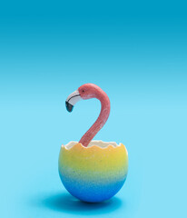 Beautiful hatch minimal concept. Awesome pink flamingo heads pop out from just broken funky yellow and marine blue egg shells. Creative copy space above with bright blue background © DPA