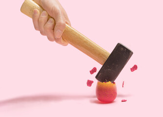 Minimal destruction concept. Male hands strike with massive hamer little glitter pink colored eggs. Beautiful pink background © DPA