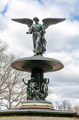 Angel of the Waters Sculpture close-up, front view from low angle at Bethesda Fountain during winter, Central Park New York, Sky with clouds in the background, vertical