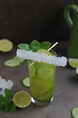 Green cucumber cocktail with sea salt and lime in a glass on a dark table. Food styling of refreshing drinks.
