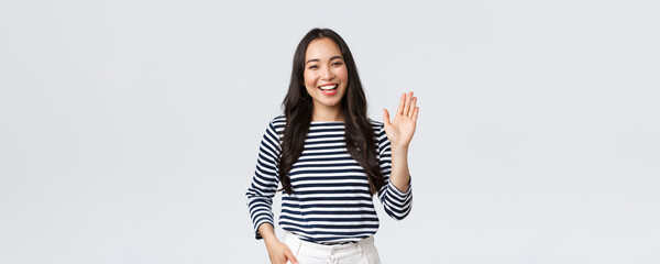 Lifestyle, people emotions and casual concept. Friendly cheerful asian woman smiling, saying hi and waving hand to greet person, make hello gesture, welcome someone - obrazy, fototapety, plakaty