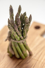 There is a bunch of fresh green delicious asparagus on the kitchen board. vertical frame