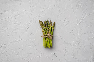 A bunch of fresh asparagus tied with twine lies on a gray background 