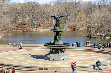 Bethesda Fountain with Angel of the Waters Sculpture with people walking and standing around the fountain, lake in the background Central Park New York during winter, horizontal