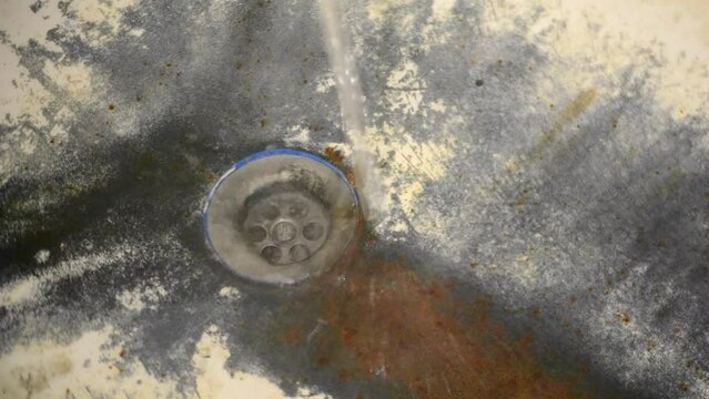 Very old rusty shabby bath close-up. A bath with peeling white enamel. Water flows in an old dirty bathtub. Black rusted dirty bath. Drain water in the rusty bathroom.
