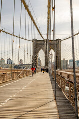 People cycling and walking on Brooklyn Bridge New York City in the evening, wire ropes in the...