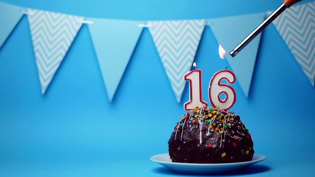 chocolate birthday cake with a burning candle number sixteen, 16 on a blue background. Copy space. place for text