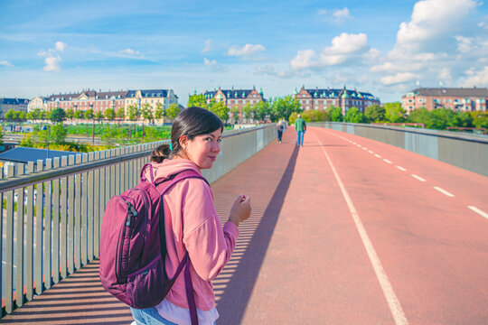 Smiling student brunette girl walking along pedestrian and bicycle bridge  across the railway  to the residential buildings. Copenhagen, Denmark