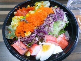 Top view of mixed vegetable salad with fresh lettuce, green oak, bread, boiled egg, flying fish and salad dressing in black bowl as a background, caesar salad, healthy food concept, Ready to eat