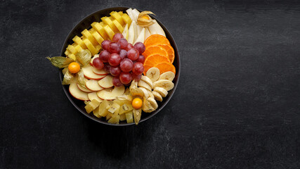 Sliced fruits on a plate, dessert. On a dark background.