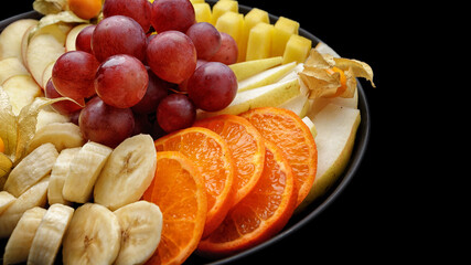 Sliced fruits on a plate, dessert. On a dark background.