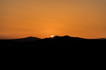 Nahaufnahme der Sonne während Sonnenuntergang über dem Horizont mit Berg Hügel Landschaft im Vordergrund, Deutschland