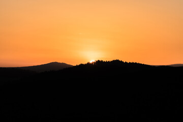 Nahaufnahme der Sonne während Sonnenuntergang über dem Horizont mit Berg Hügel Landschaft im Vordergrund, Deutschland