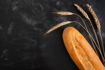 Fresh french baguette bread and wheat on a dark background. View from above