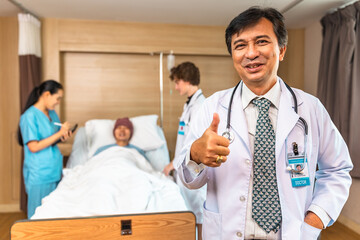 Obraz premium Young Asian elder man in medical robe smiling and looking at camera during work against at clinic.. healthcare medical checkup concept.