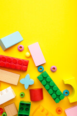 Multicolored blocks of the children's constructor lie on yellow background. Space for text