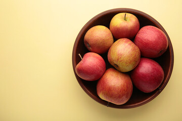 Many red apples in round bowl on beige background.