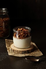 Granola with yogurt in the little glass jar, big jar with granola, dark background, low key