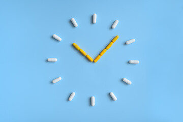 Clock made of white and yellow pills on blue background