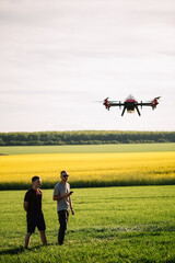 Fototapeta na wymiar Two farmers watch an agricultural drone fly and fertilize the fields