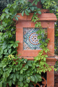Stone decorative fence pedestal painted tin-glazed ceramic tilework pattern azulejo,ornamental art panel covered with green overgrown sprout vine ivy. Portugal, Sintra, Monserrate palace park.