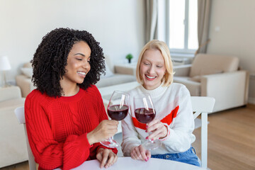 Two female friends spending time together at home, sitting on sofa. copy space. Cheerful women drinking wine