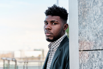 Serious and attractive African man in blazer is looking at camera in the background of the city.