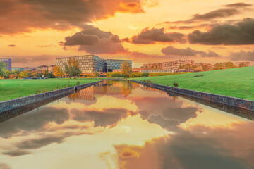 Beautiful yellow sunset with clouds over a river channel with reflection in a park overlooking residential buildings and a metro station DR Byen in the city area &Oslash;restad. Copenhagen, Denmark